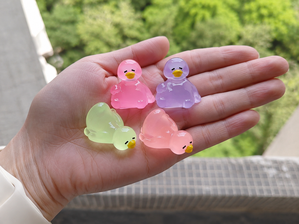 Glow in the dark colorful duck resin charms displayed on hand